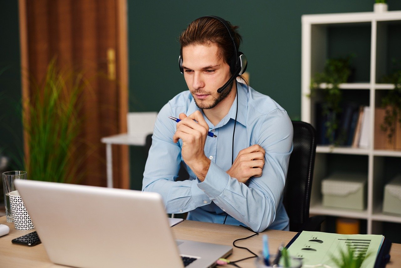 Man sitting in his home office, smiling and feeling satisfied while talking on the phone.